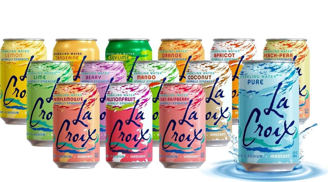 Twelve colorful La Croix sparkling water cans in various flavors, including lemon, lime, orange, tangerine, key lime, berry, mango, coconut, passionfruit, apricot, peach-pear, and pure, are displayed together.