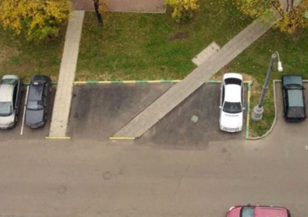 Aerial view of a parking lot with cars parked on both sides; a sidewalk cuts diagonally through the middle, making several parking spaces unusable.