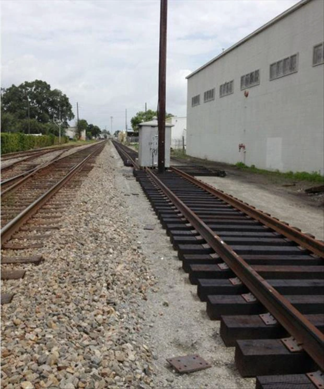 Railroad tracks running parallel, with one set abruptly ending at a utility pole, causing the rails to stop while the other set continues straight along a building under a cloudy sky.