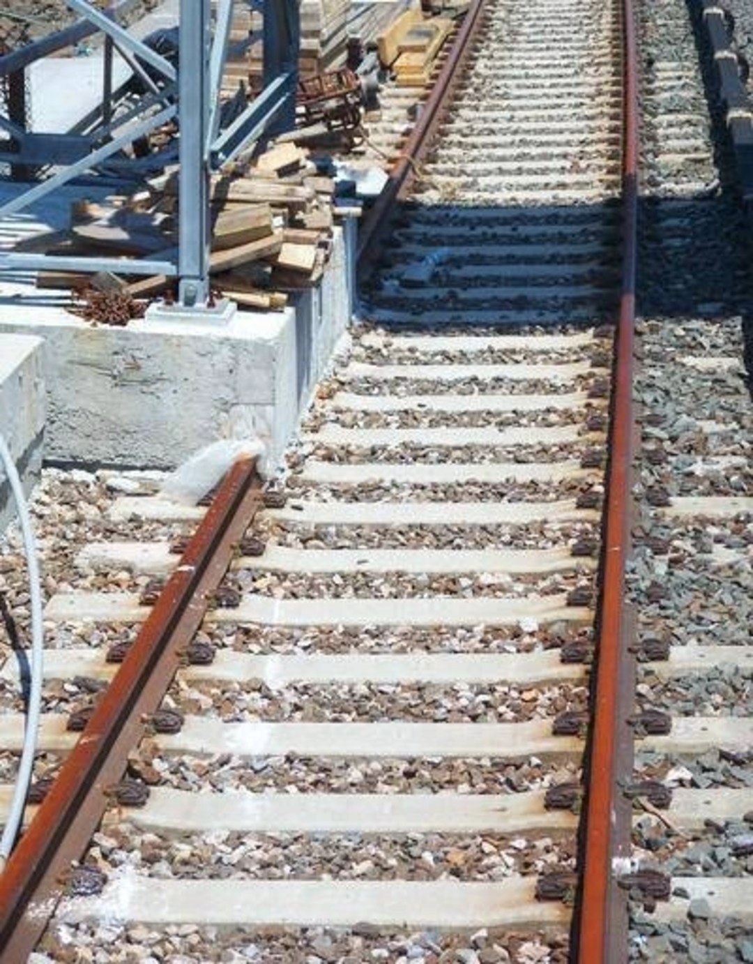 A railway track with unevenly spaced and crooked sleepers, surrounded by gravel and construction materials, creating a distorted and unsafe appearance.