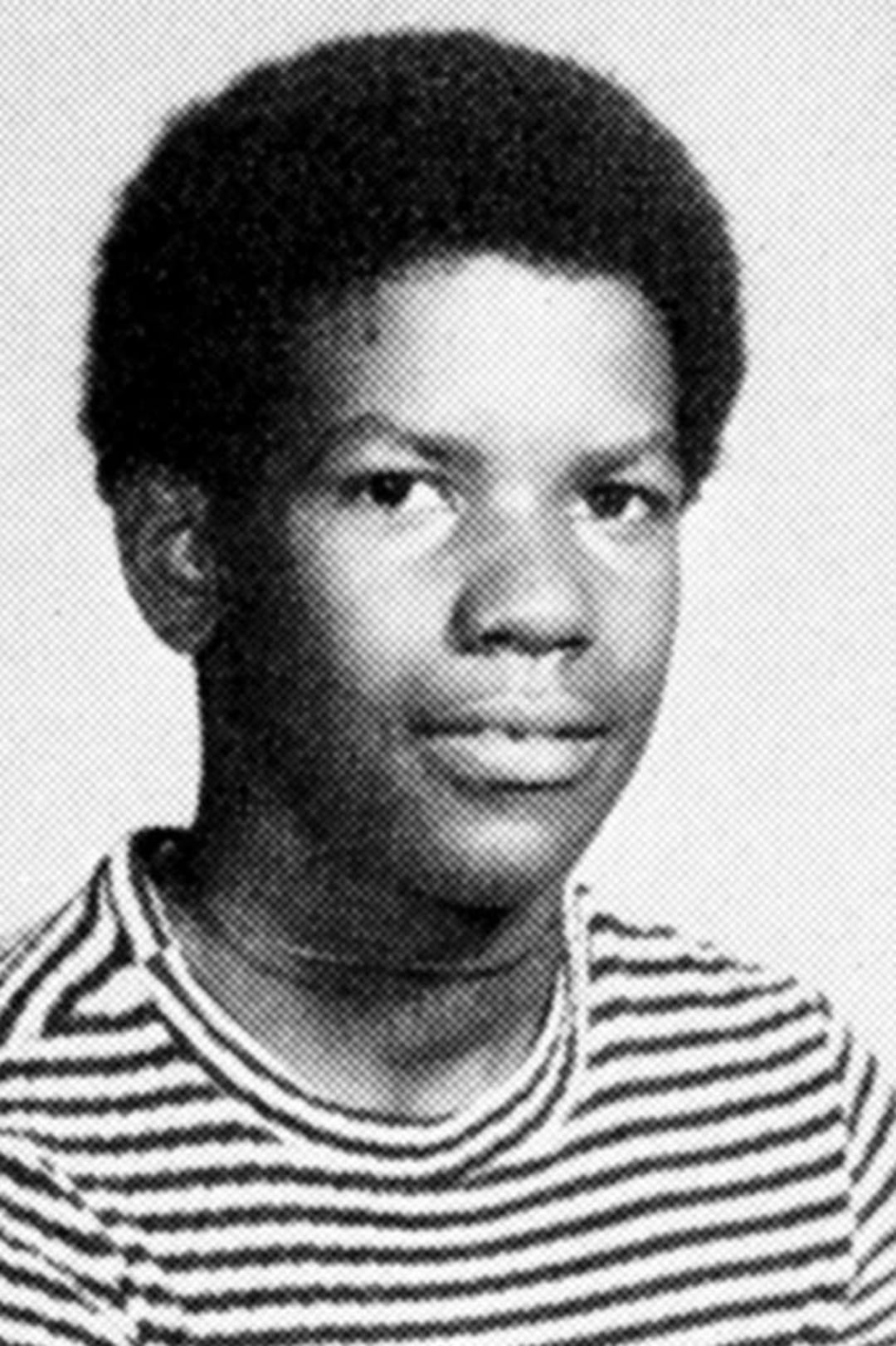 Black and white yearbook-style photo of a young boy with short curly hair, wearing a striped t-shirt, looking directly at the camera with a neutral expression.