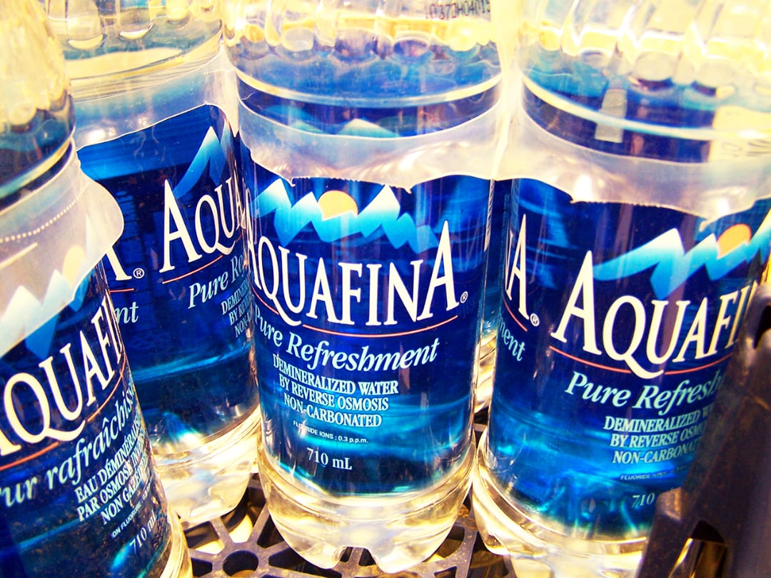 Close-up of several Aquafina bottled water containers, showing clear plastic bottles with blue and white labels, placed together on a black metal shelf.