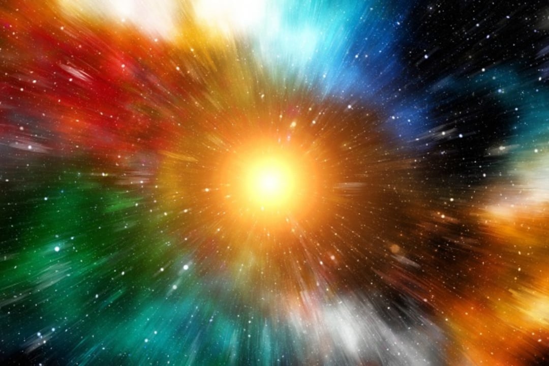 A bright explosion of yellow and orange light at the center, with streaks of red, green, blue, and white radiating outward, set against a dark star-filled space background.