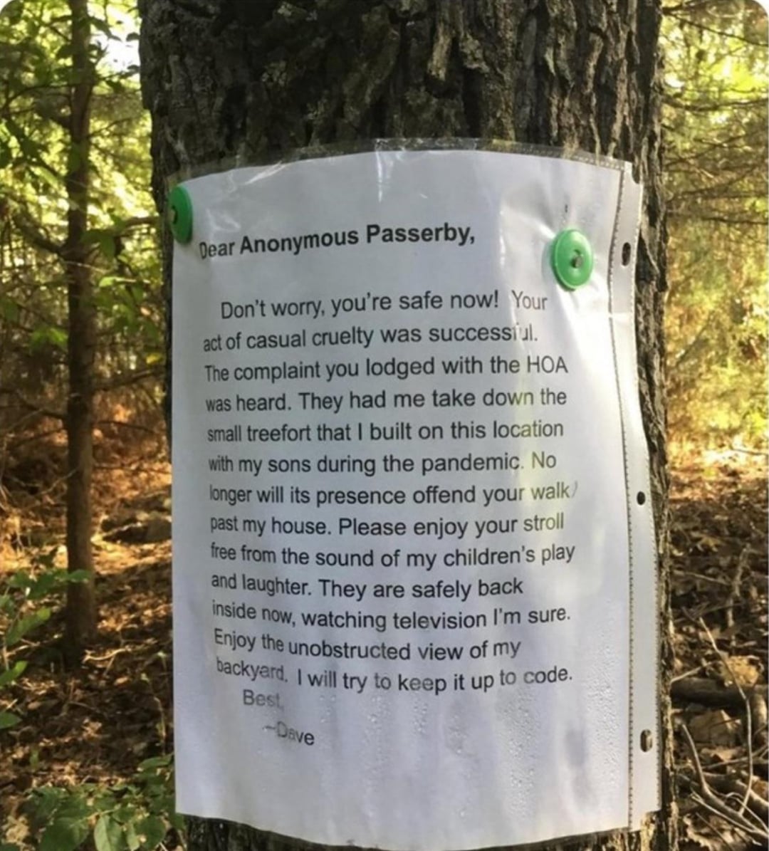 A letter is pinned to a tree in a wooded area with green pushpins. The typed note sarcastically thanks an anonymous passerby for complaining to the HOA about a small treehouse, which has since been removed.