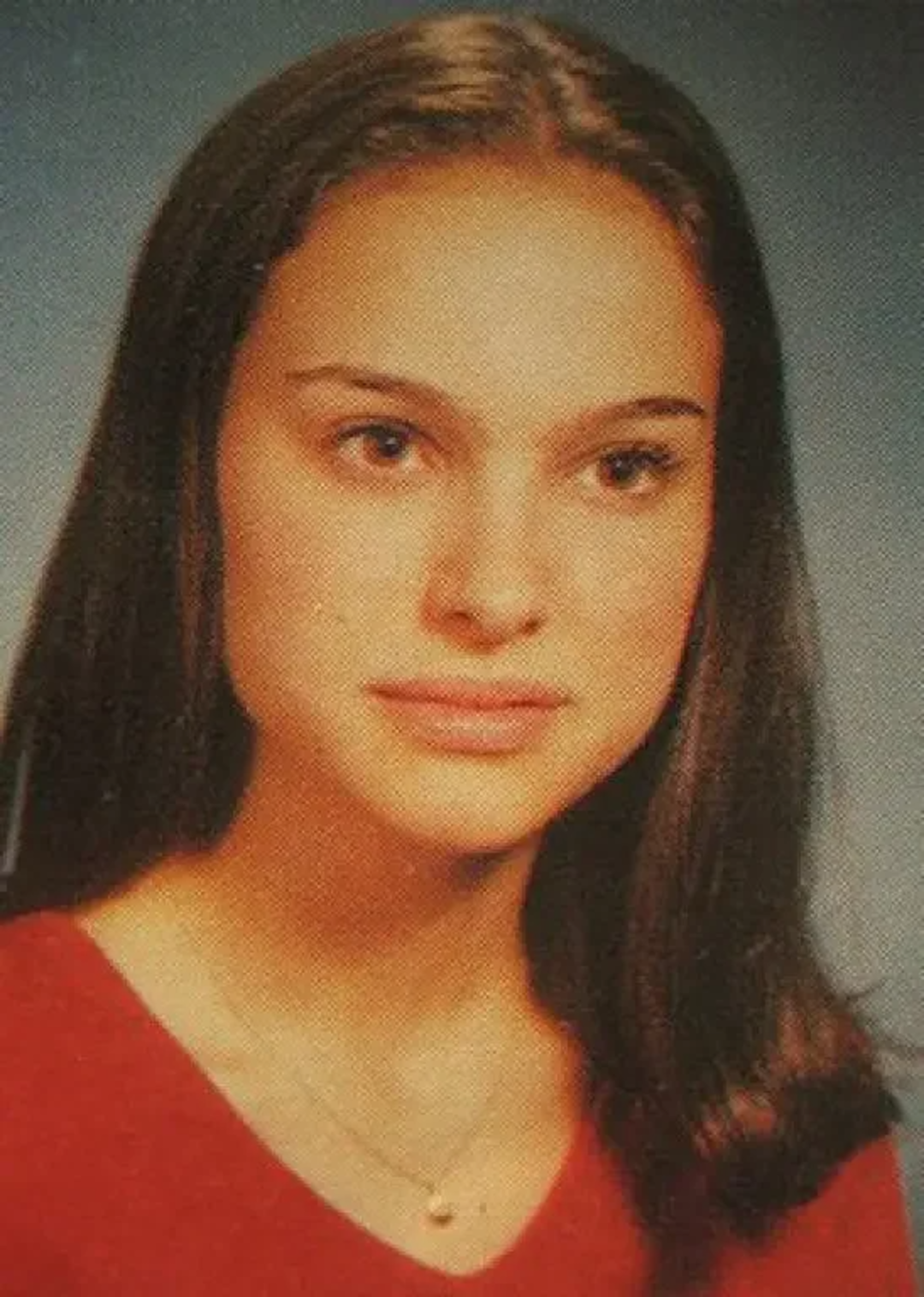 A young woman with straight, dark brown hair, wearing a red top and a delicate necklace, poses for a school portrait against a blue background. She has a calm expression and looks slightly to the side.