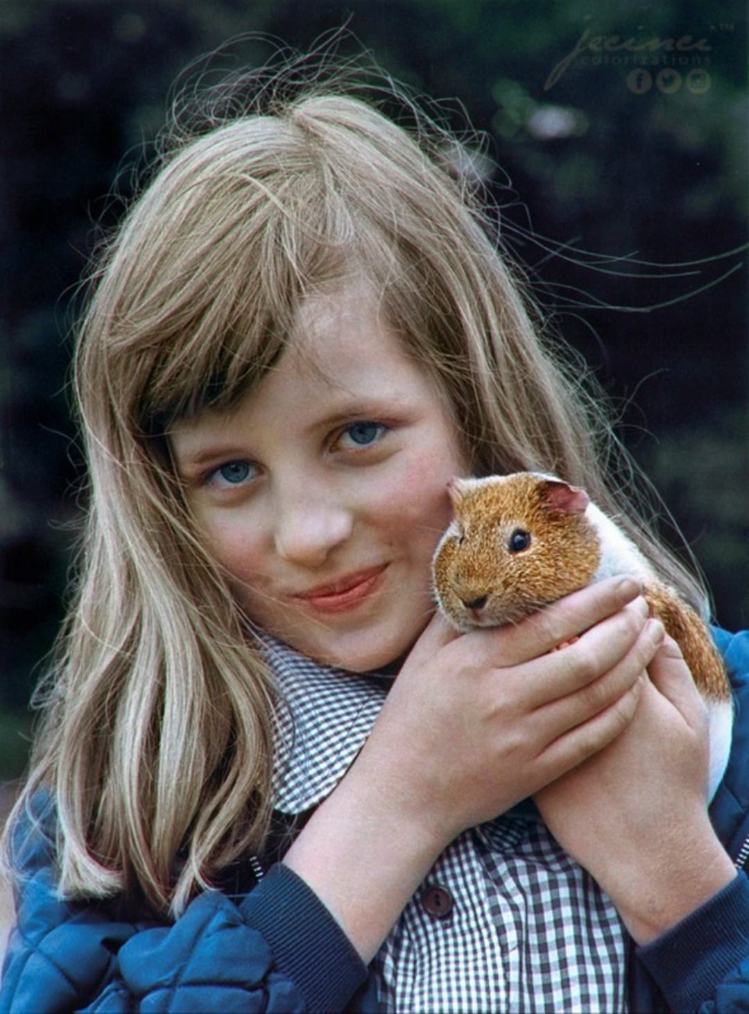 A young girl with long blonde hair and blue eyes smiles at the camera while gently holding a brown and white guinea pig in her hands, outdoors with greenery in the background.