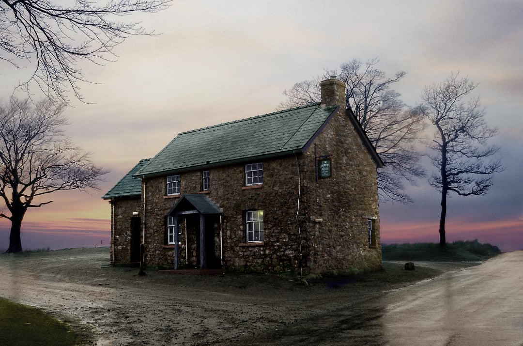 A stone house with a green roof stands at a crossroads surrounded by bare trees under a cloudy, pastel-colored sunset sky. The ground is muddy, and the scene feels quiet and isolated.