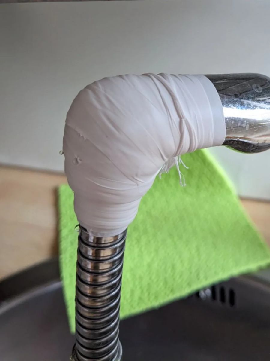 A kitchen faucet with its curved joint wrapped in white tape, likely as a temporary repair. A green cloth is draped over the sink in the background.