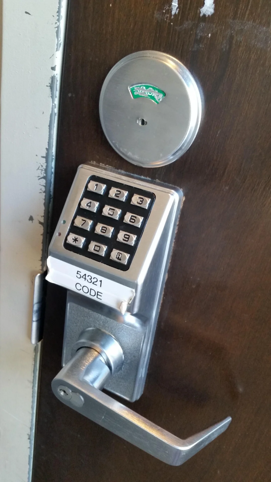 A close-up of a door with a keypad lock. The keypad has numbered buttons, and a label beneath it reads "54321 CODE." The door handle is below the keypad, and a deadbolt is above.