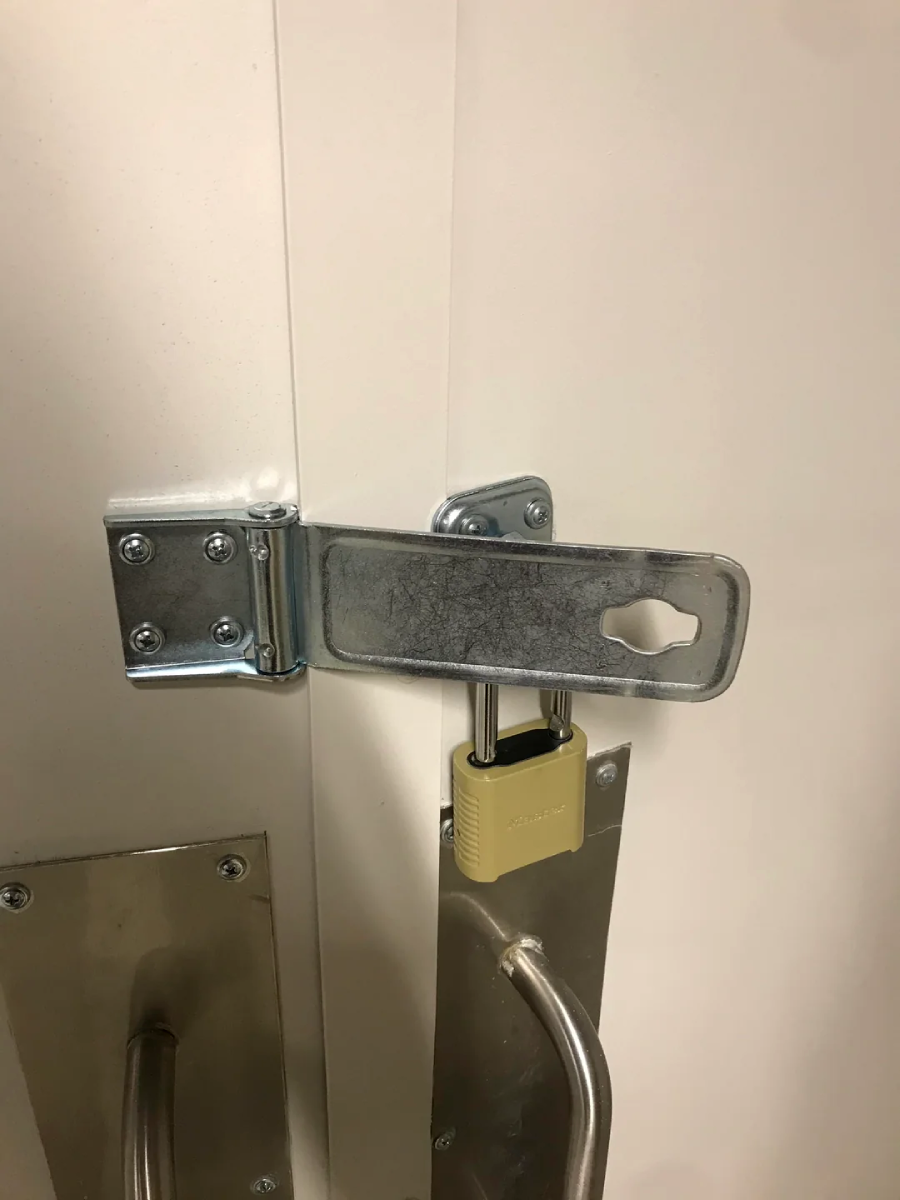 A metal latch is secured with a padlock, but the latch is not actually locking the double doors; it is placed over the handles in a way that does not prevent the doors from being opened.