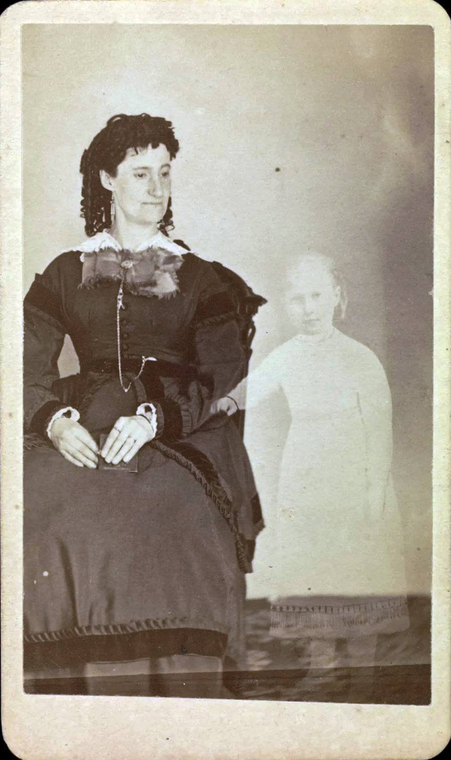 A vintage sepia photograph shows a seated woman in Victorian-era clothing, with a faint, ghostly image of a young girl standing beside her, creating a supernatural effect.