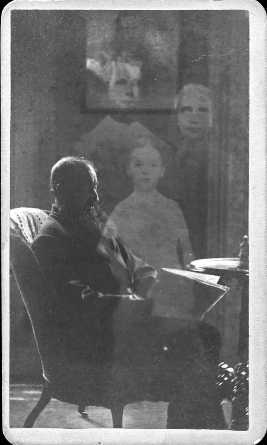 A bearded man sits in a chair reading, with the faint, ghostly images of three children appearing above and behind him in the background. The photo is black and white and has an eerie, vintage quality.