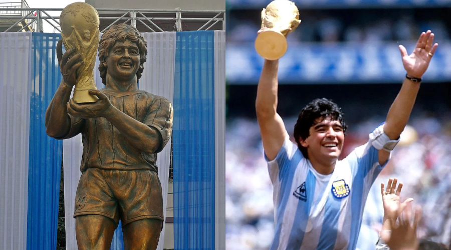 A bronze statue of Diego Maradona holding the World Cup trophy stands beside a photo of Maradona in an Argentina jersey, lifting the same trophy and waving to cheering fans.
