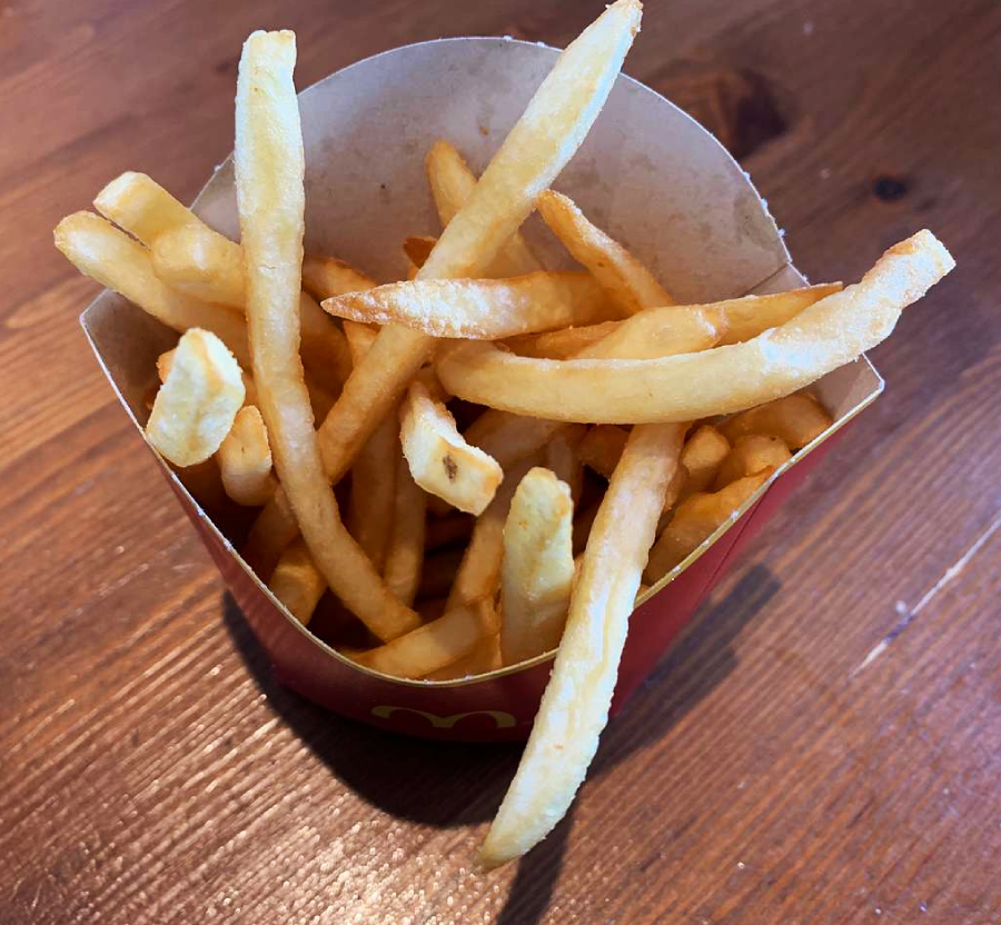 A red carton filled with golden, crispy French fries sits on a wooden table.