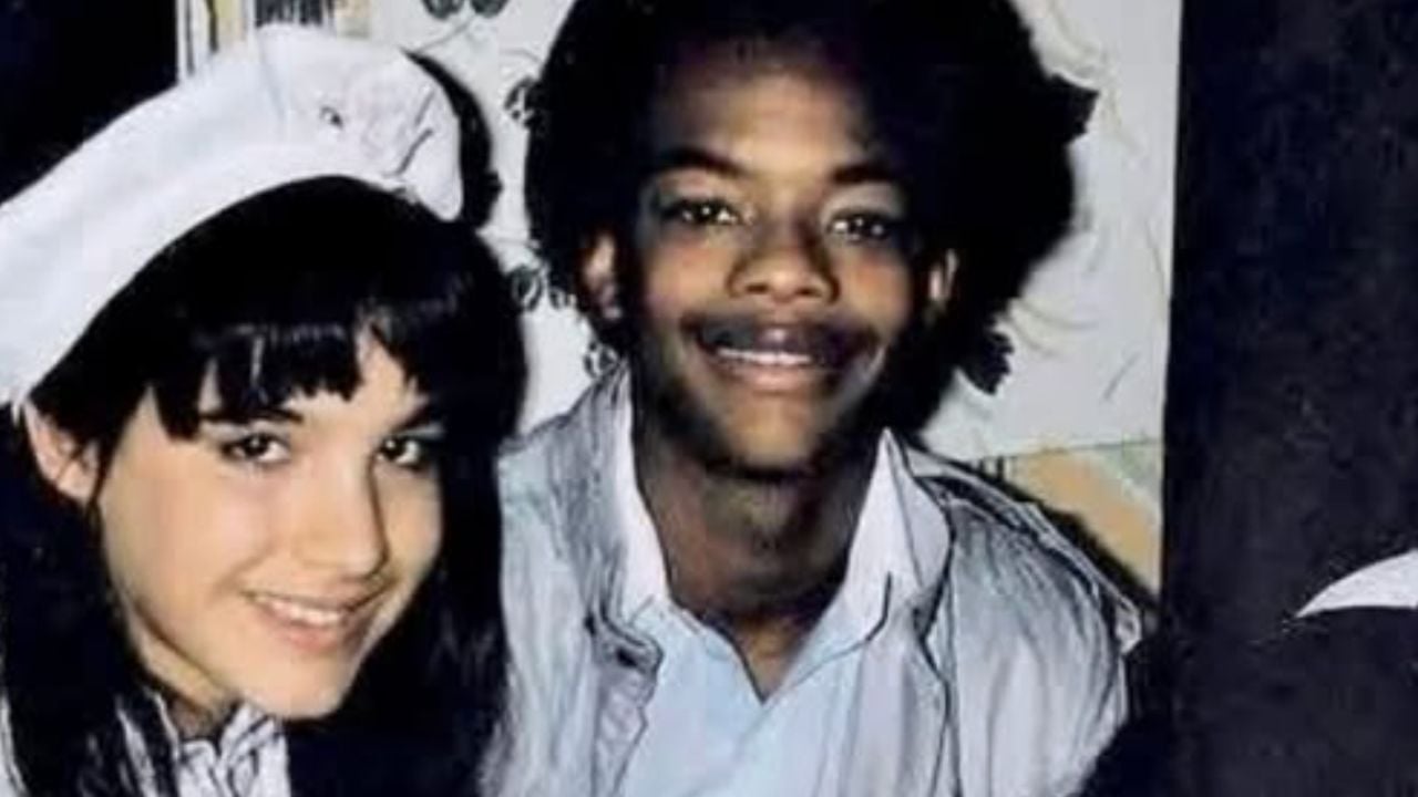 Two teenagers smiling at the camera. The girl on the left has long dark hair with bangs and is wearing a white hat. The boy next to her has short curly hair and is wearing a light-colored shirt.