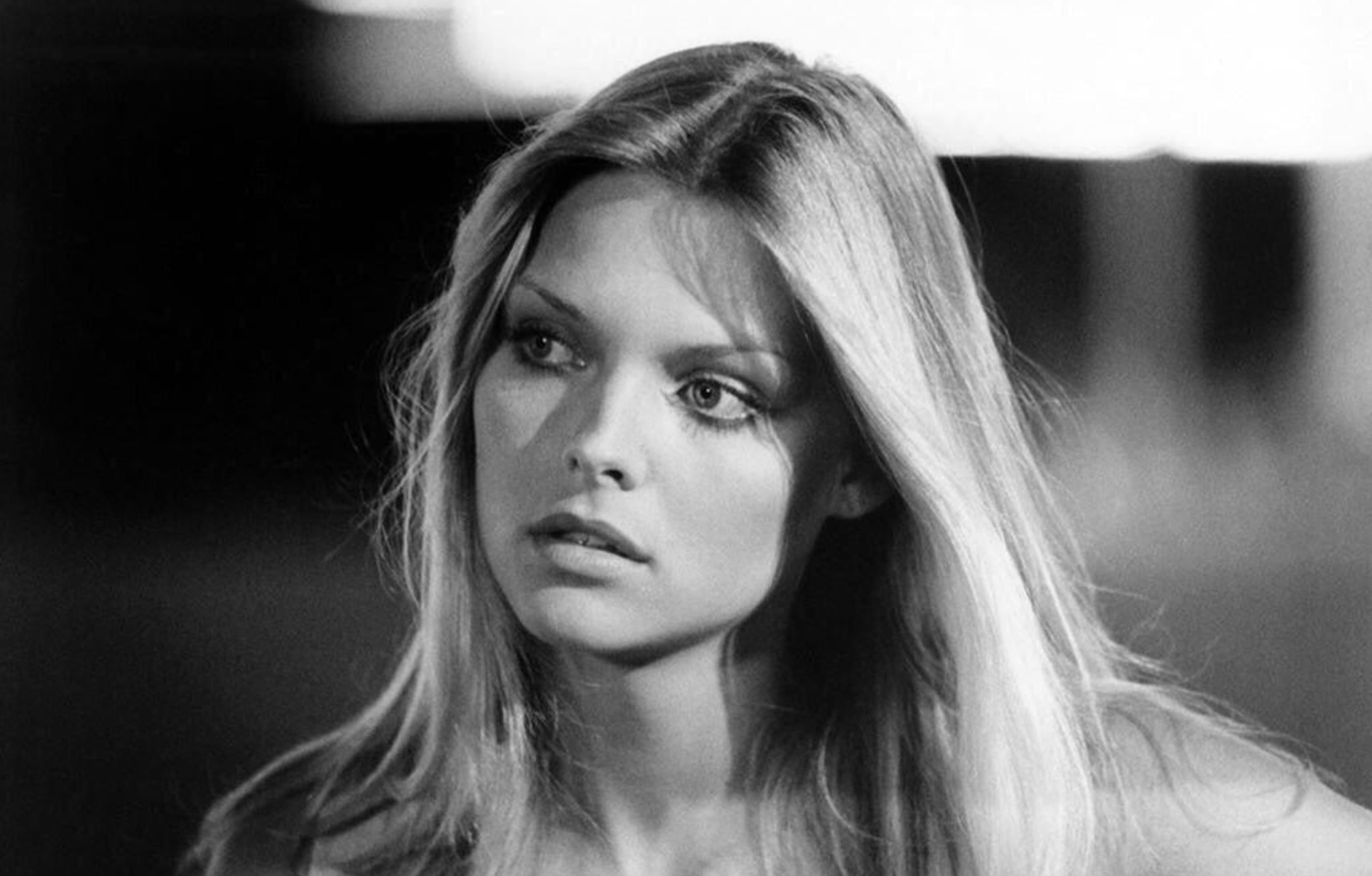 A black and white photo of a young woman with long, straight hair, looking slightly to the side with a neutral expression. The background is blurred, highlighting her facial features.