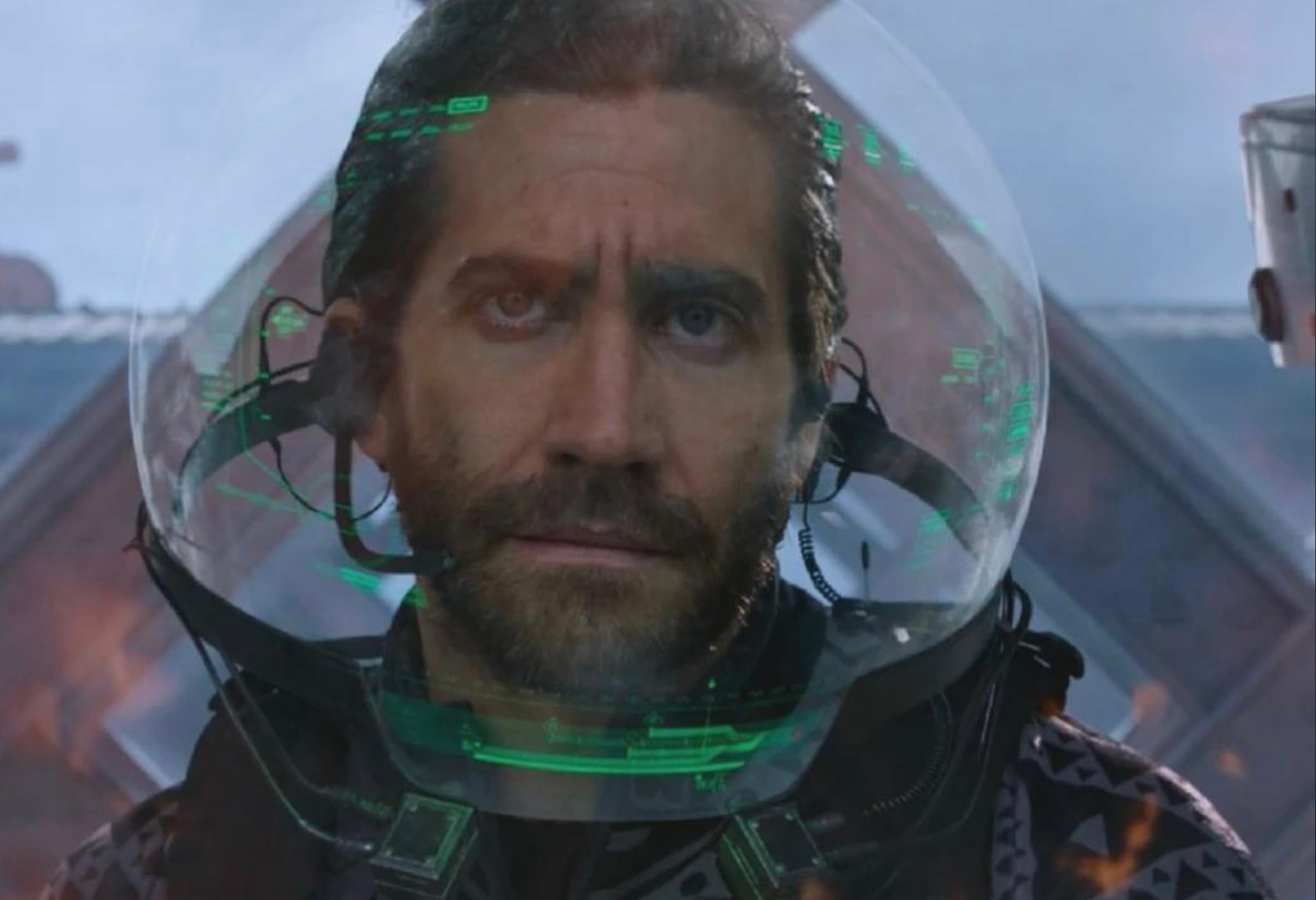 A man with a serious expression wears a transparent helmet with digital green displays projected on the visor, suggesting a futuristic or sci-fi setting. Geometric shapes and reflections are visible in the background.