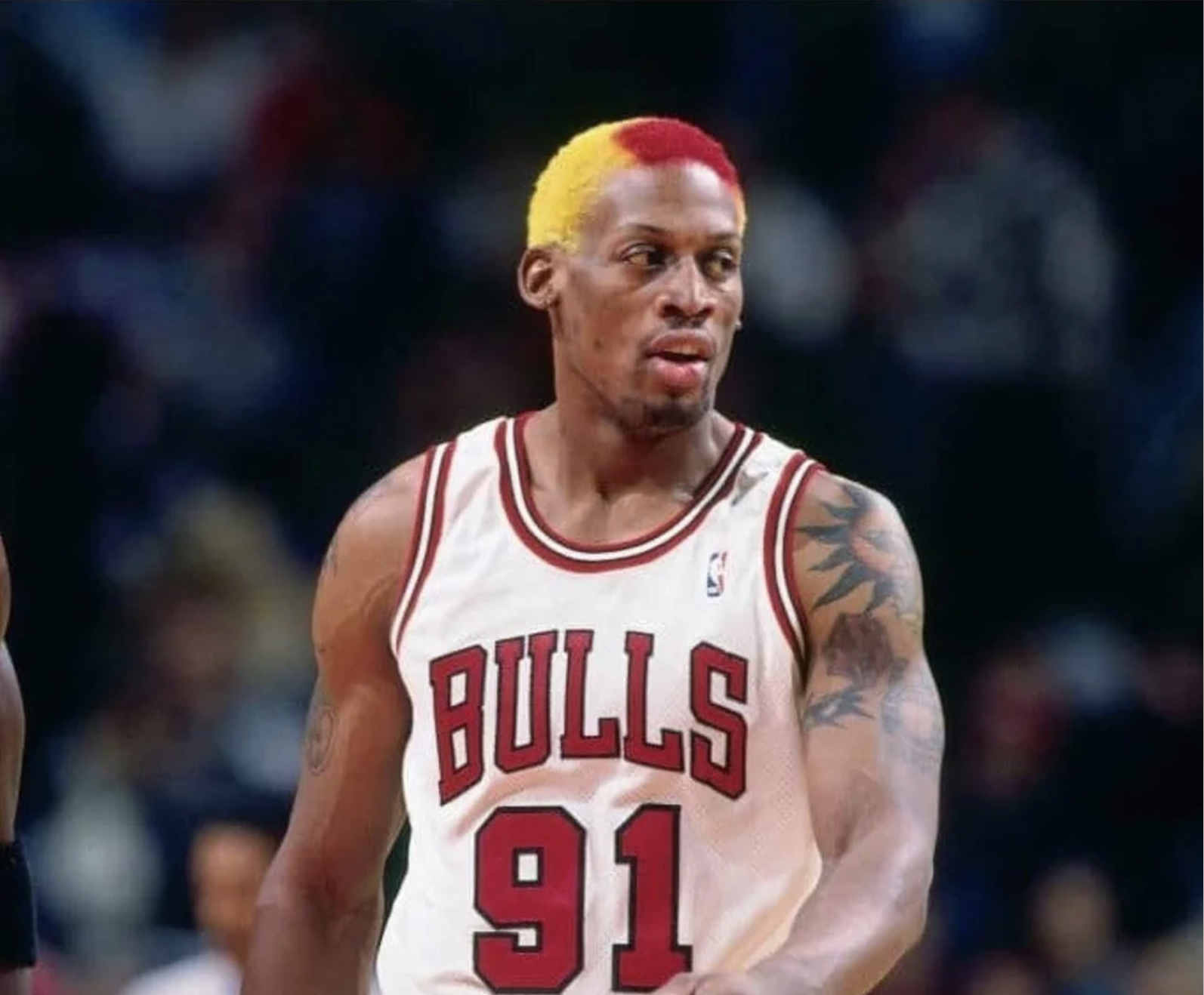 A basketball player wearing a Chicago Bulls jersey with the number 91, sporting a yellow and red dyed hairstyle, stands on the court during a game.