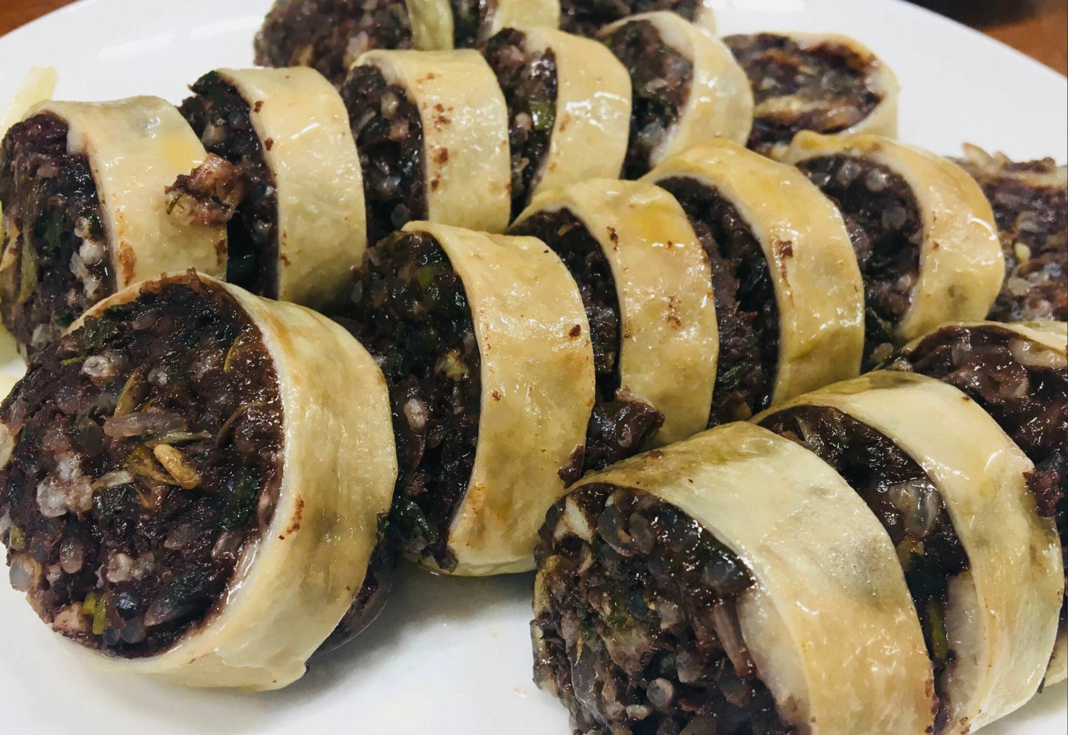 Close-up of sliced Korean blood sausage (soondae) arranged on a white plate, showing the dark, rice-and-noodle-stuffed filling wrapped with a light-colored casing.