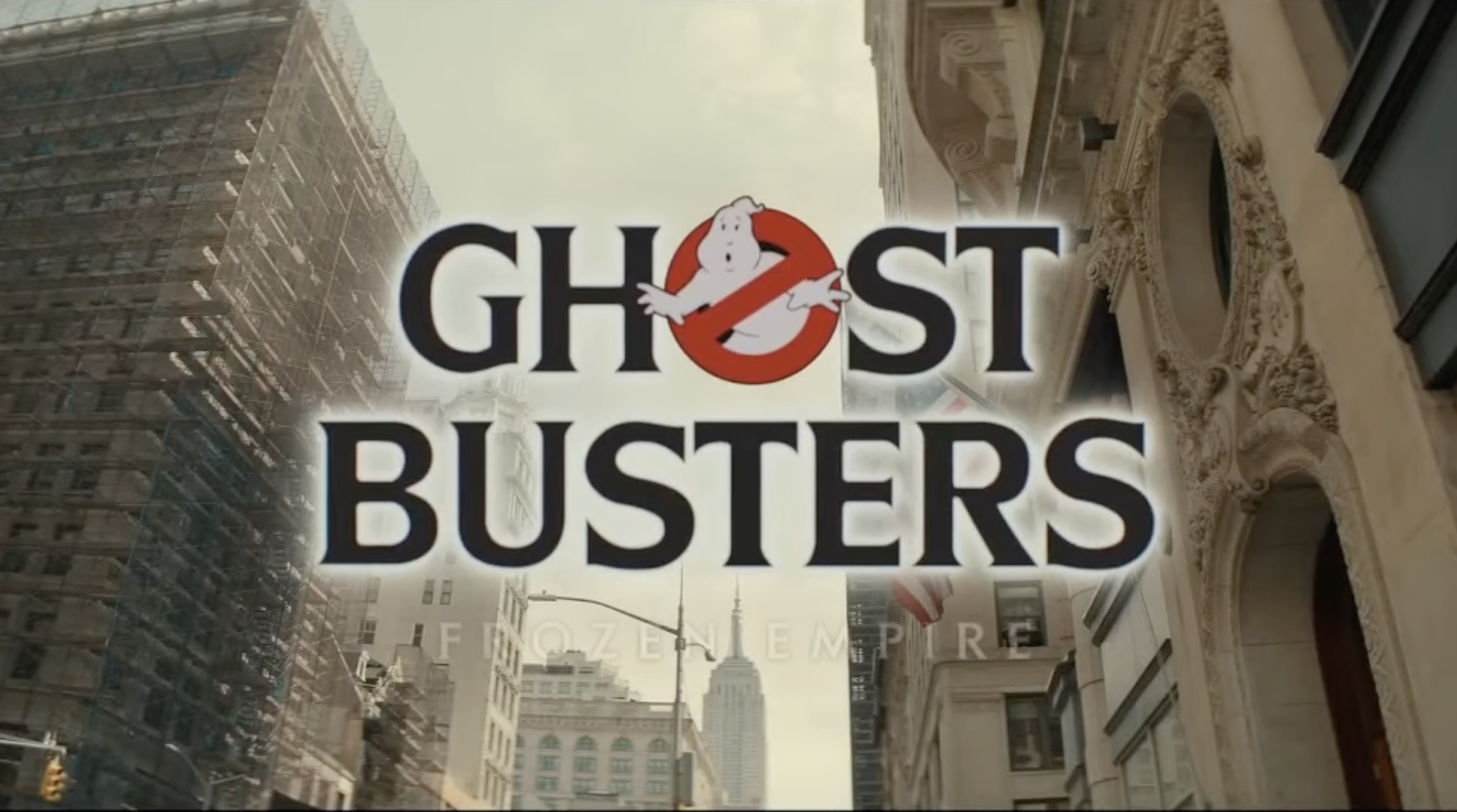 The Ghostbusters logo with a red “no ghosts” symbol and the word “Ghostbusters” appears over a city street with tall buildings and scaffolding, with “Frozen Empire” faintly visible below the logo.
