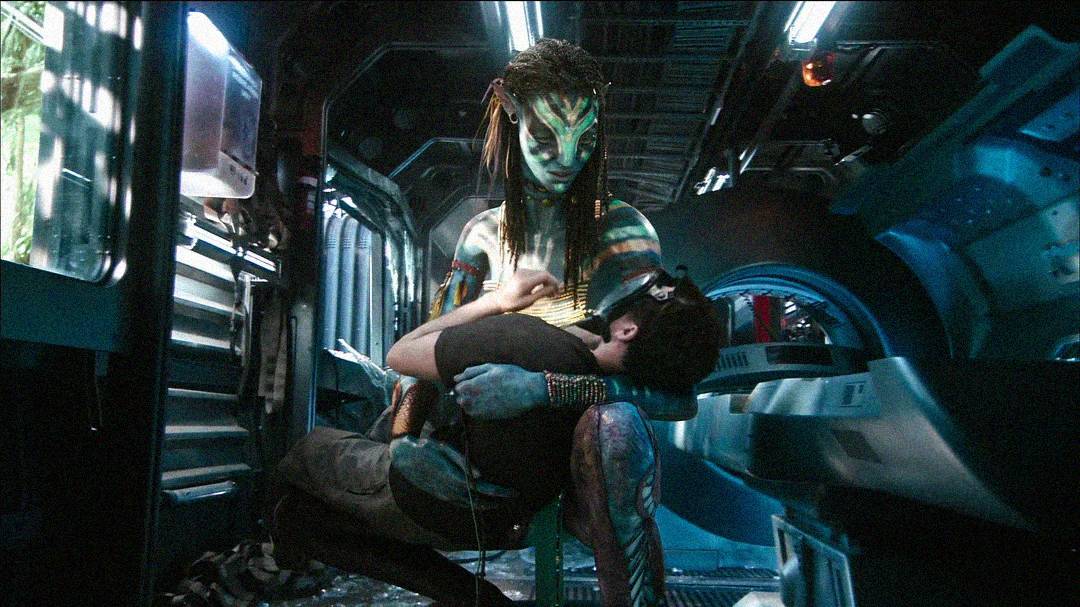 A tall, blue, humanoid alien cradles a human in her arms inside a futuristic, metallic spaceship, with dim lighting and advanced technology visible in the background.