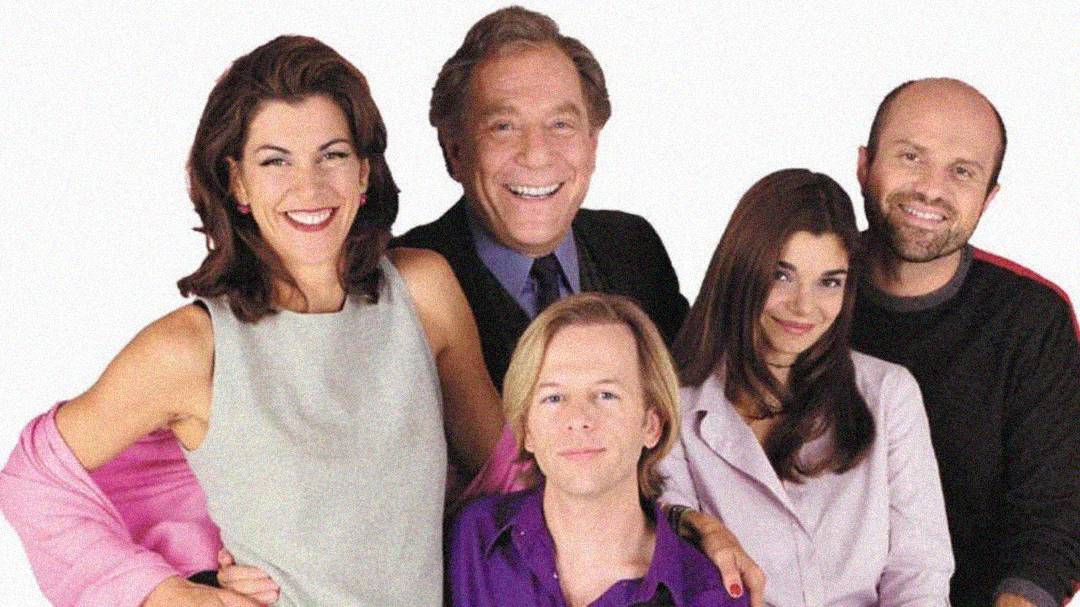 Five people pose together, smiling against a plain white background. Three are standing at the back, and two are seated in front. They appear to be a group of colleagues or friends, dressed in business-casual attire.