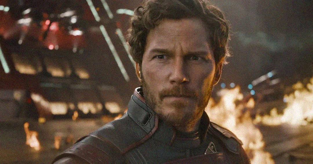 A man in a futuristic suit stands in front of flames and metallic structures, looking serious and intense in a dramatic sci-fi setting.