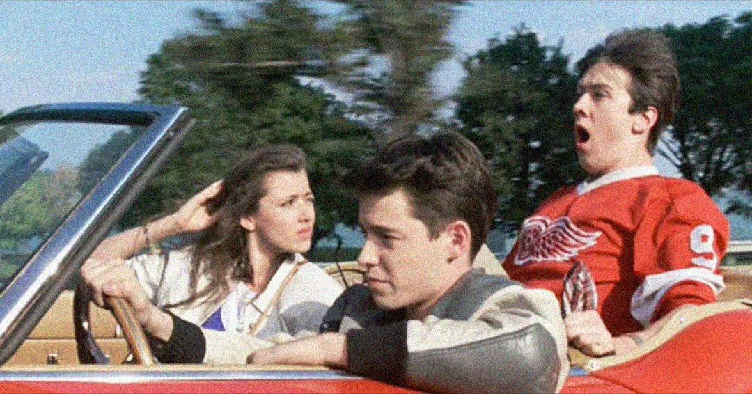 Three young people ride in a red convertible. The driver looks ahead calmly, the passenger beside him looks back, and a passenger in the back seat wearing a red jersey appears surprised or excited. Trees blur in the background.