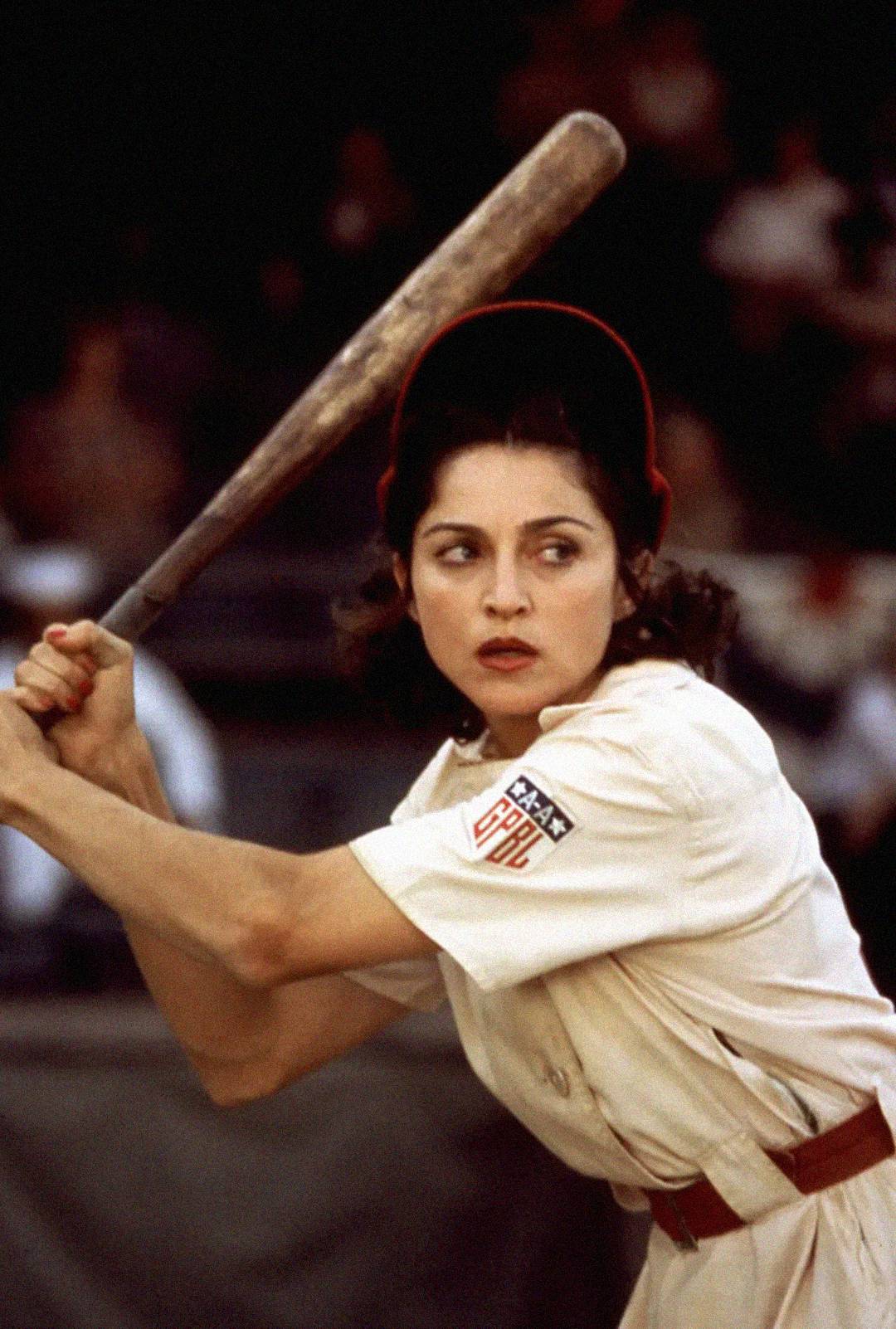 A woman in a vintage baseball uniform and red cap stands ready to bat, focusing intently at home plate during a game.