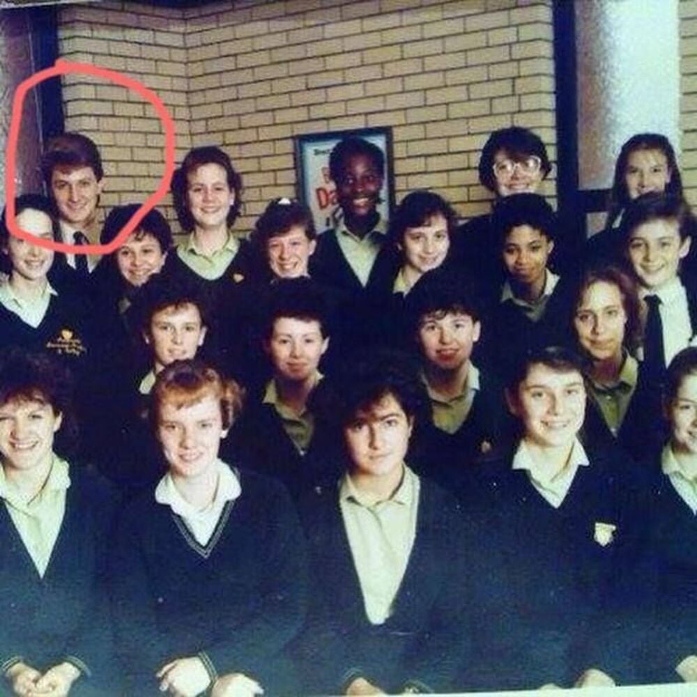 Old class photo of a group of school students in uniform posing indoors; one student in the back row is circled in red.