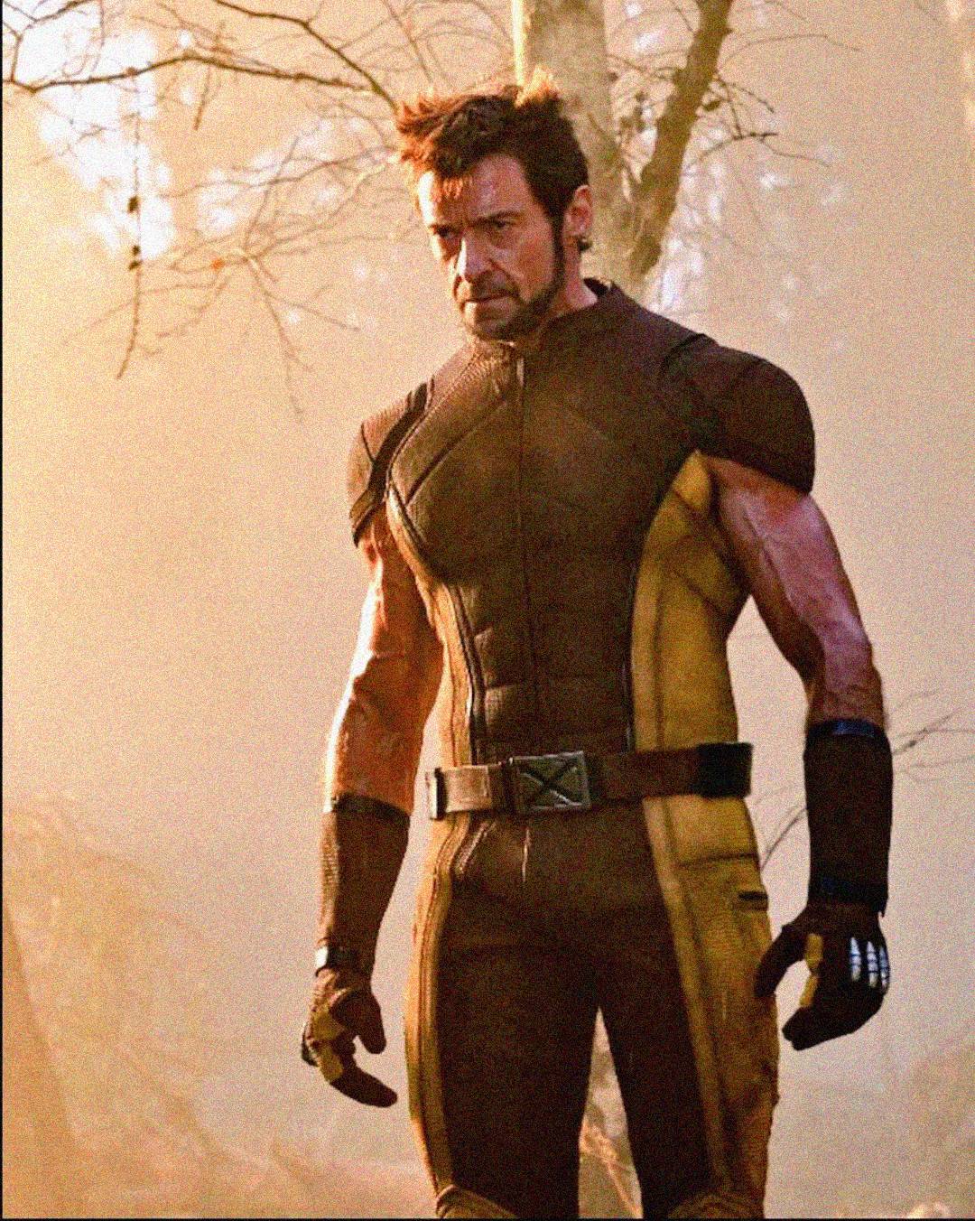 A man in a yellow and brown superhero costume stands in a wooded area with sunlight filtering through the trees, looking serious and focused.