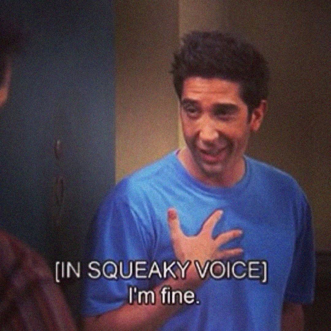 A man in a blue shirt touches his chest and forces a smile, with the caption “[IN SQUEAKY VOICE] I’m fine.” appearing at the bottom of the image.