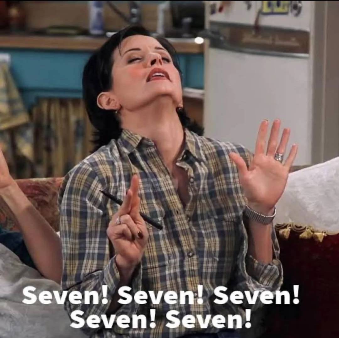 A woman in a plaid shirt sits on a couch with her eyes closed and head tilted back, holding up seven fingers. The text on the image reads, "Seven! Seven! Seven! Seven! Seven!