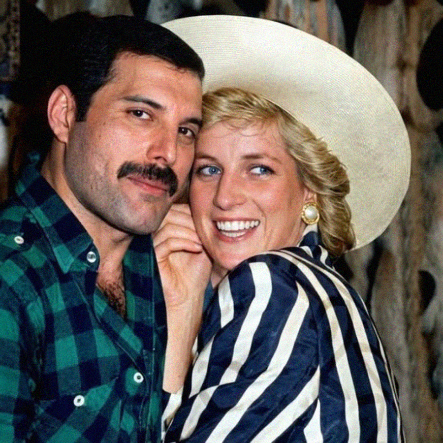 Two people pose closely together. The person on the left has short dark hair, a mustache, and wears a green plaid shirt. The person on the right has blonde hair, a wide-brimmed hat, and a striped jacket, smiling at the camera.