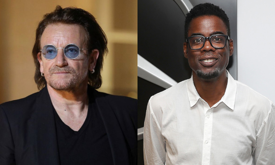 Two men side by side; on the left, a person with medium-length hair, beard, blue-tinted glasses, and a dark jacket; on the right, a person with short hair, glasses, and a white shirt, smiling at the camera.