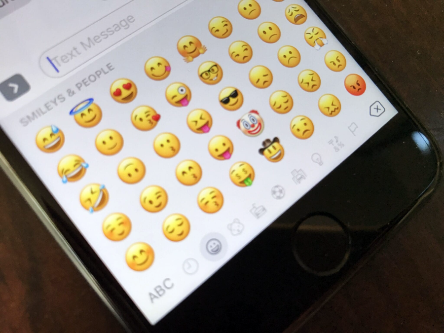 A smartphone screen displays the emoji keyboard open to the "Smileys & People" section, showing various yellow face emojis in rows above the keyboard.