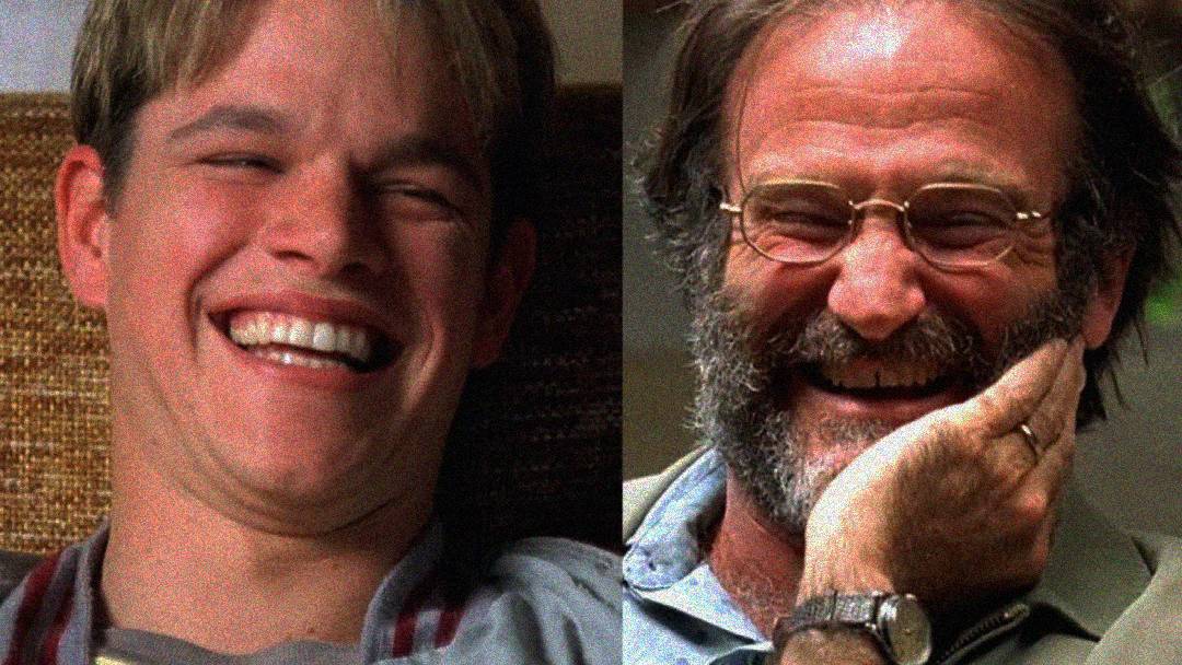 Two men are side by side, both smiling and laughing warmly. The man on the left has short blonde hair and wears a casual shirt, while the man on the right has glasses, a beard, and holds his hand to his face in amusement.