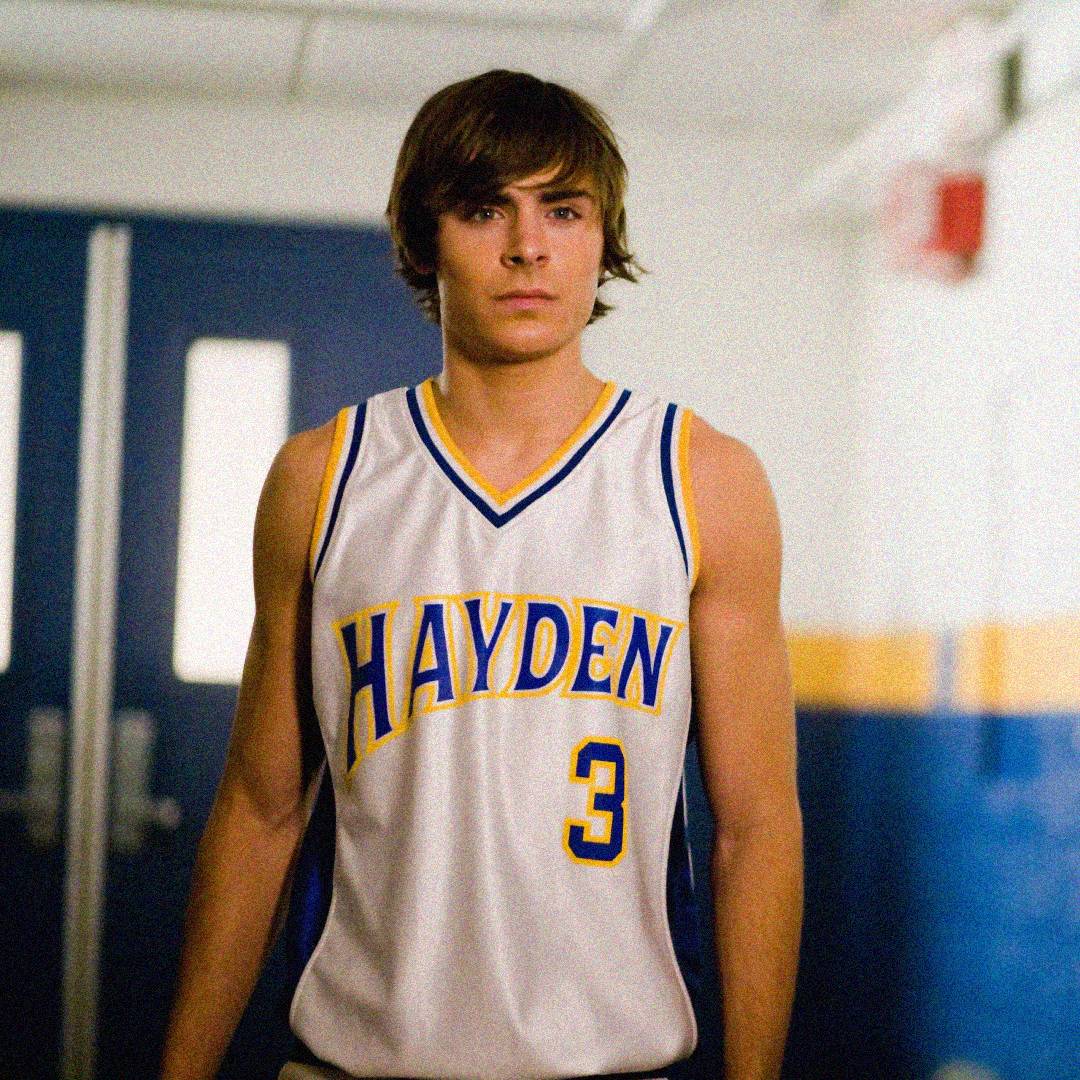 A young man wearing a white basketball jersey with blue and yellow trim, labeled "HAYDEN" and the number 3, stands in a hallway with blue doors and a yellow and blue wall behind him.