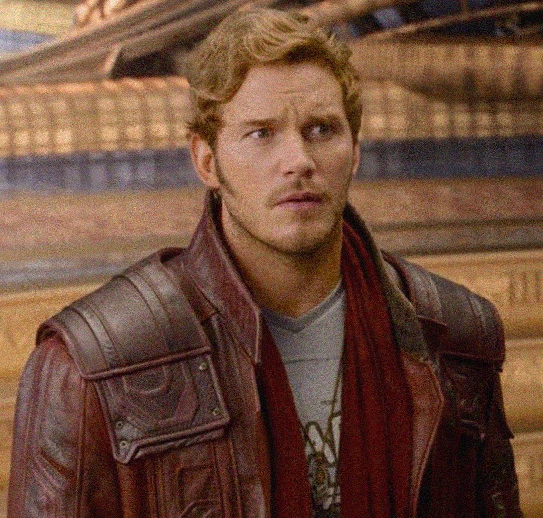 A man with wavy blond hair wears a maroon leather jacket and a light gray shirt, looking slightly confused. The background appears to be the interior of a spacecraft or futuristic setting.