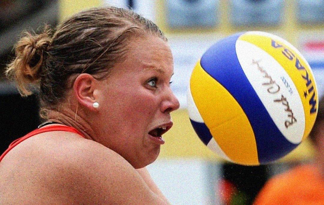 A woman with a shocked expression flinches as a volleyball comes very close to her face during a game.