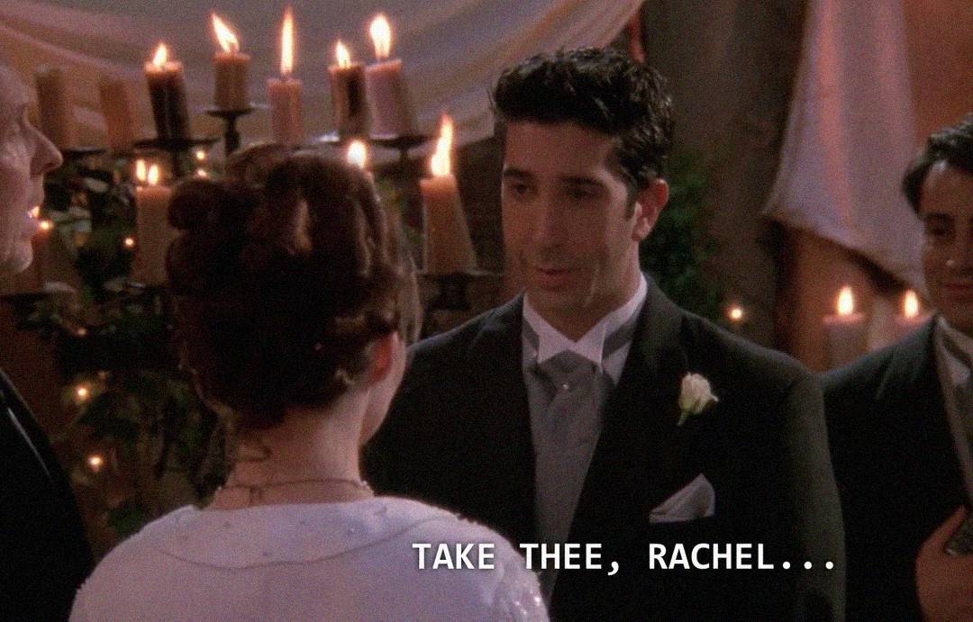 A groom in a tuxedo stands facing a bride in a white dress during a wedding ceremony, with candles and drapes in the background. Subtitle reads: "TAKE THEE, RACHEL...