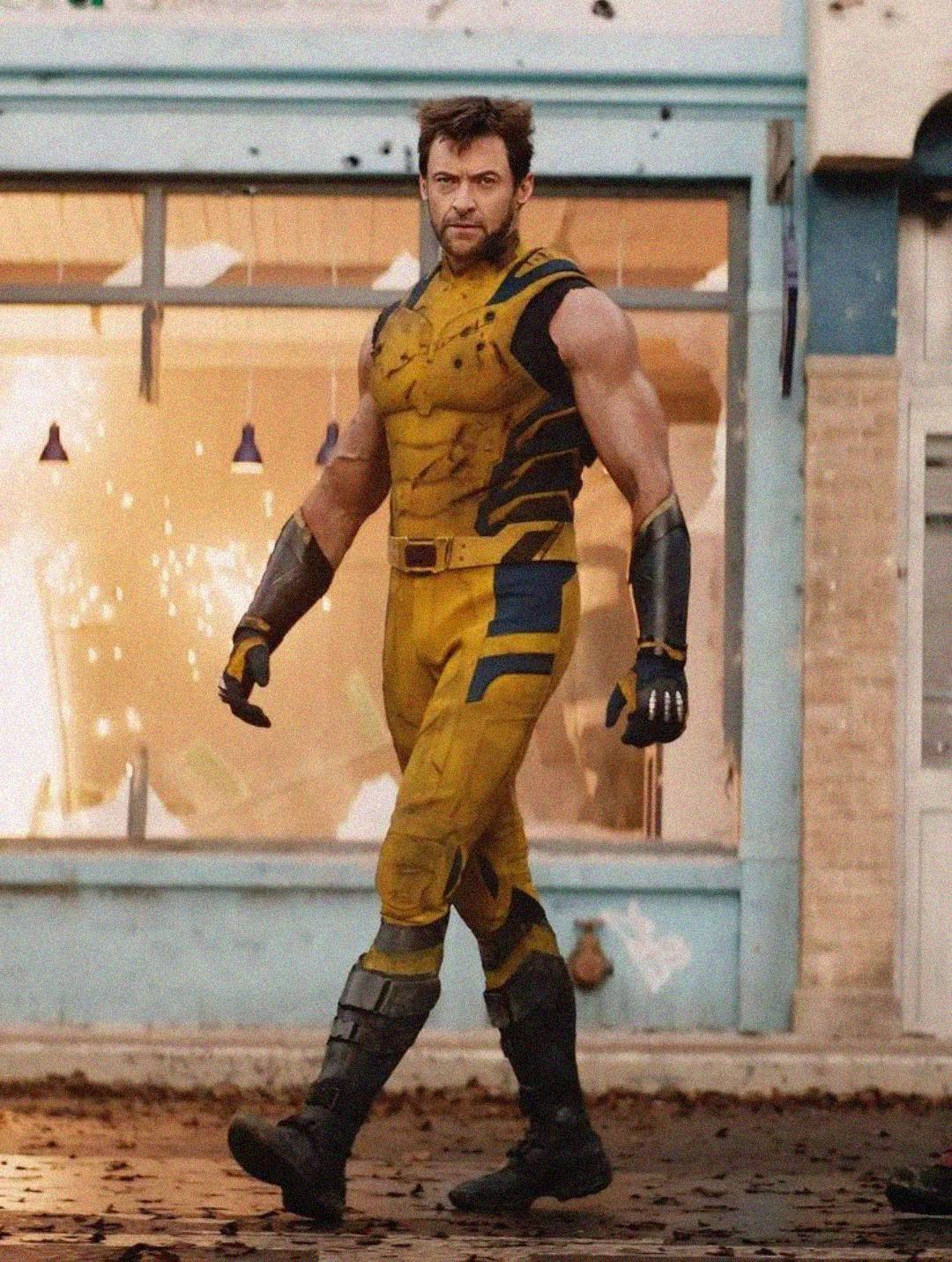 A muscular man in a yellow and blue superhero costume confidently walks outside a damaged building with shattered windows and broken glass scattered around.