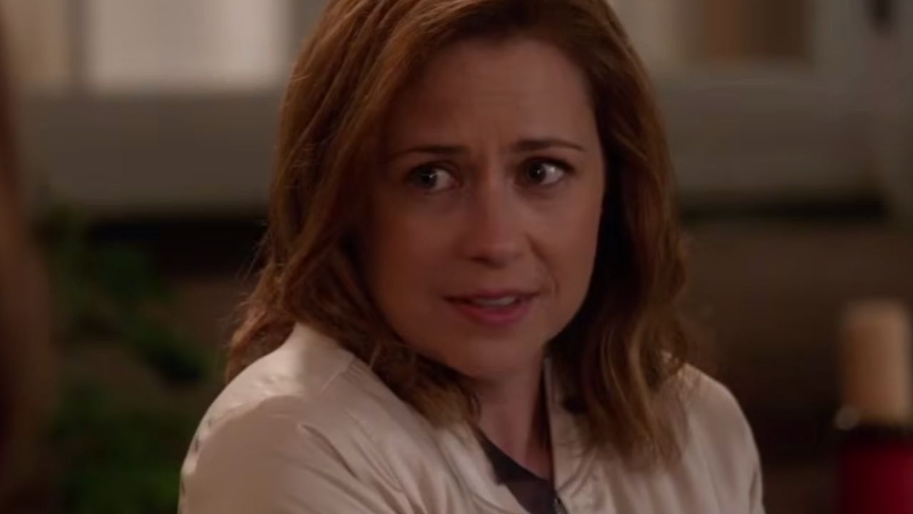 A woman with shoulder-length brown hair looks slightly concerned while sitting indoors, wearing a light-colored jacket.