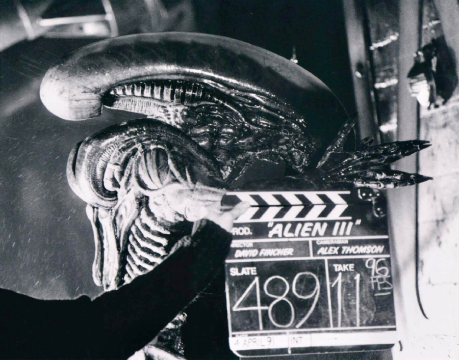 A person holds a clapperboard reading "Alien III" in front of a detailed alien creature on a movie set, preparing for a scene. The clapperboard lists David Fincher as director and Alex Thomson as cinematographer.