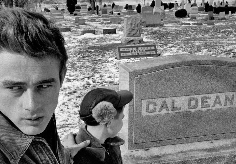 A young man and a boy stand in a snowy cemetery near a gravestone that reads "CAL DEAN." The young man looks off to the side with a serious expression while the boy faces the gravestone.