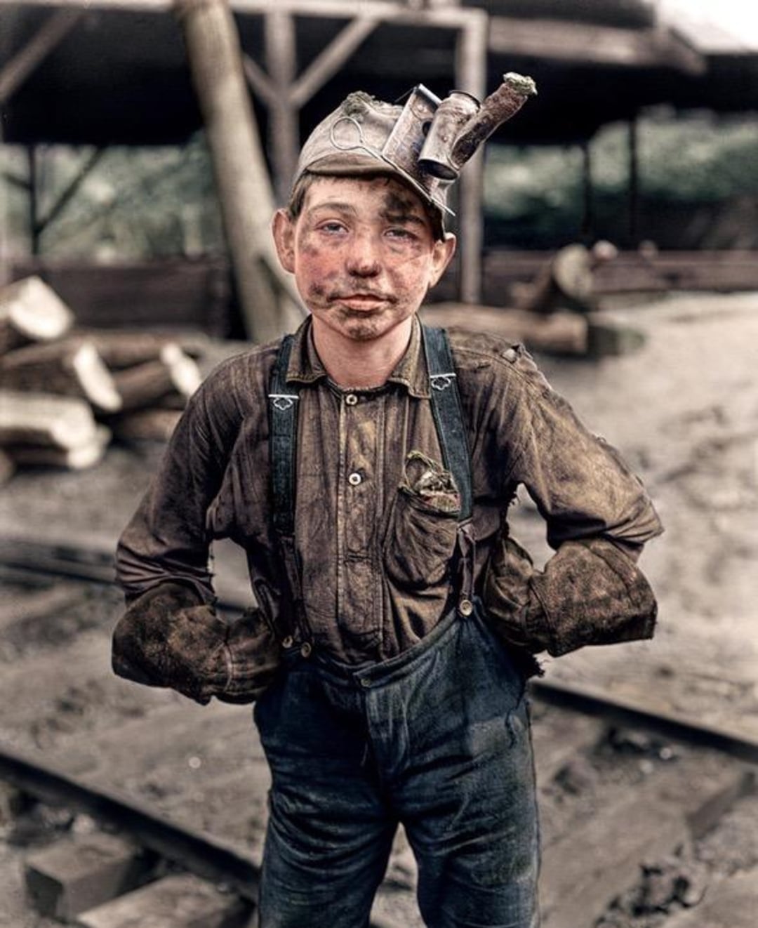 A young boy miner stands with hands on hips, wearing dirty overalls and a miner’s cap with a light. His face and clothes are smudged with dirt, and industrial equipment is visible in the background.