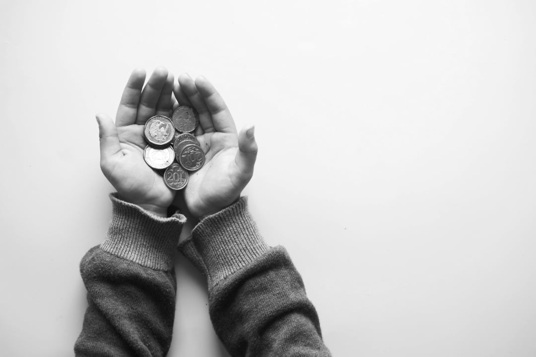 A pair of hands in long sleeves holds several coins against a plain, light background in a black-and-white photo.