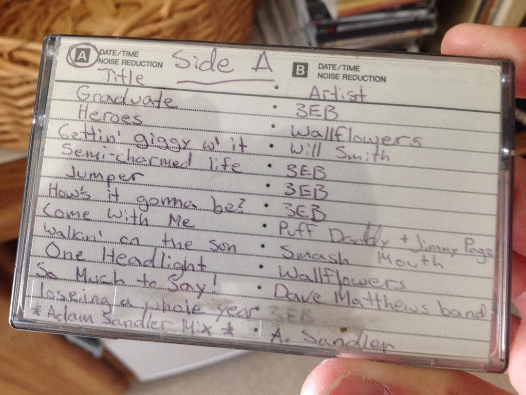 A handwritten mixtape tracklist labeled "Side A" with songs by 3EB, Wallflowers, Will Smith, Dave Matthews Band, and others, inside a cassette case held by a person's hand.