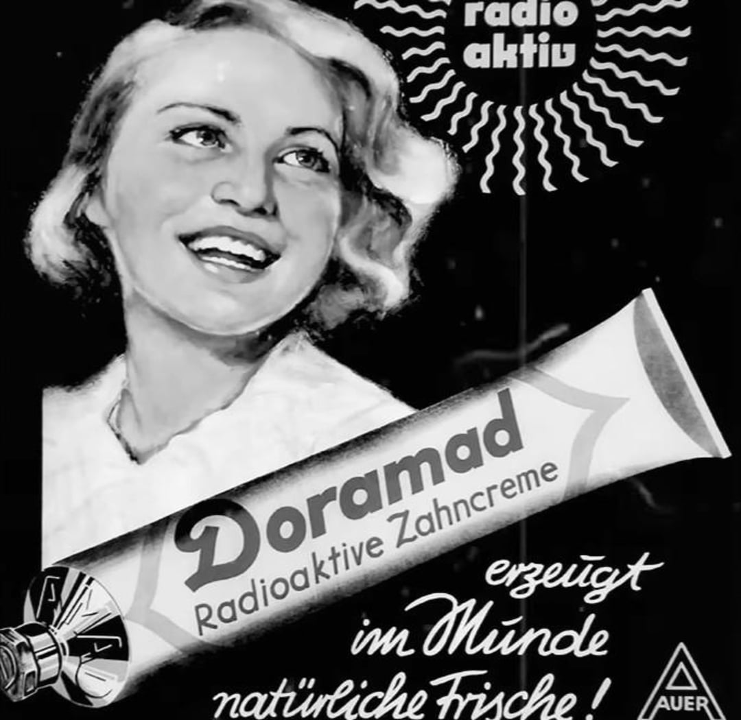 A vintage black-and-white advertisement features a smiling woman next to a large toothpaste tube labeled "Doramad Radioaktive Zahncreme," with German text promoting its freshness and a small "Auer" logo in the corner.