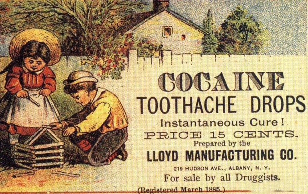 A vintage advertisement shows two children playing outside and promotes "Cocaine Toothache Drops" as an instant cure, priced at 15 cents, prepared by Lloyd Manufacturing Co., and available at druggists.